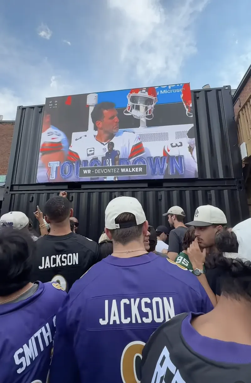 Ravens fans in jerseys under the 18-foot jumbotron on the Purple Patio